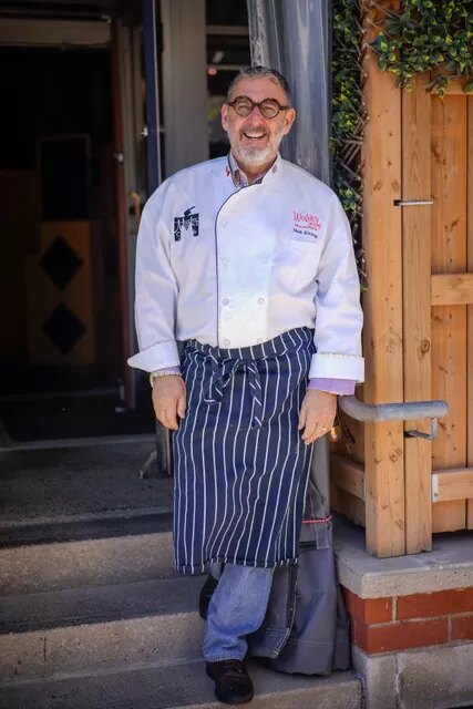 Chef Mark Kitching in his whites and a striped apron at the door of Waldo’s
