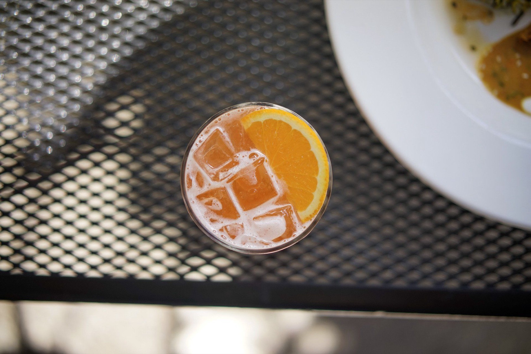 An orange-garnished cocktail over ice on the patio table