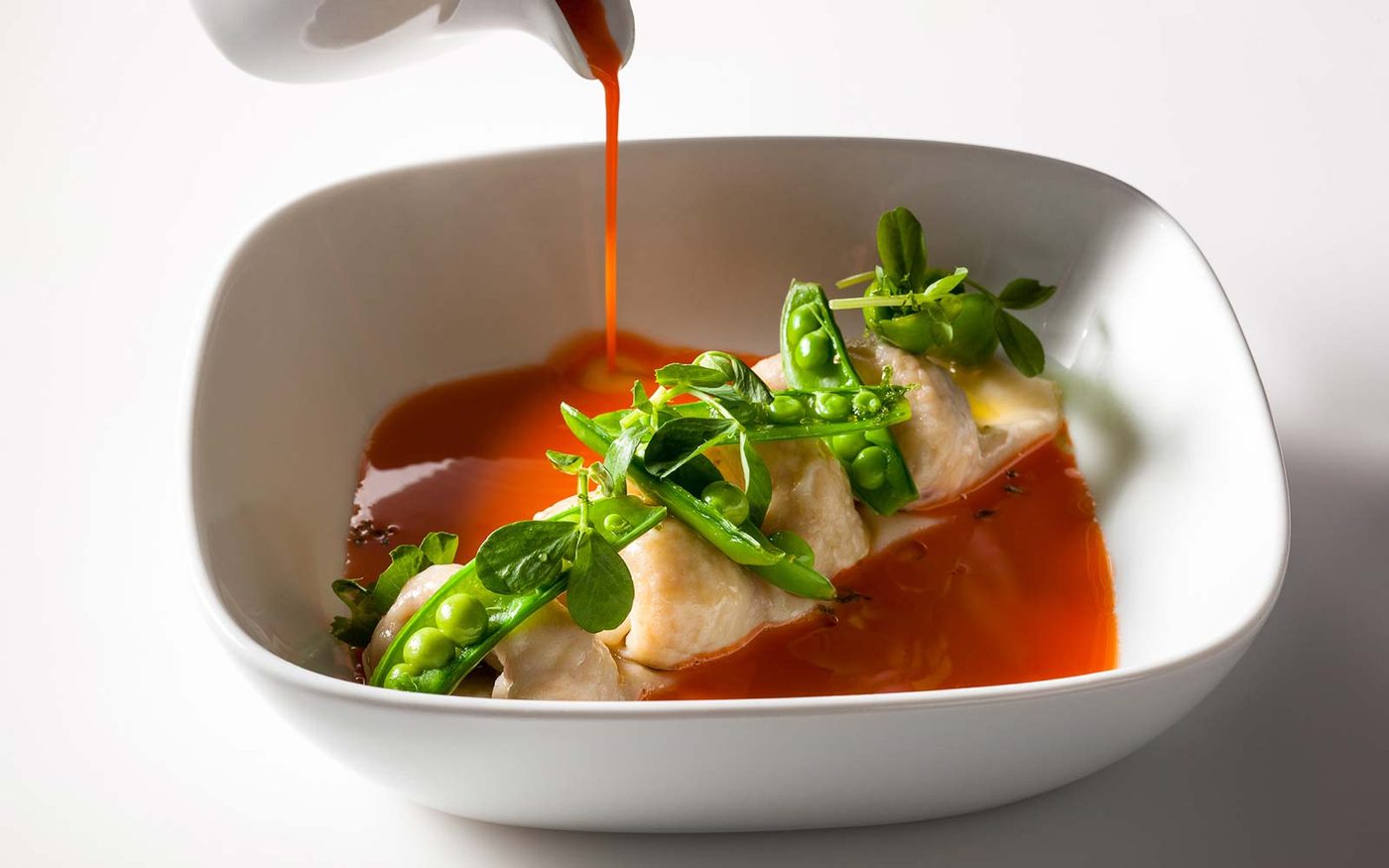 Poached white fish with peas and a red pepper broth poured at the table